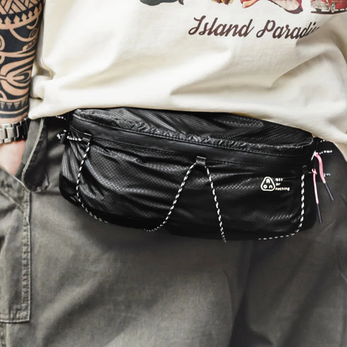 Person wearing a black waist bag with visible branding on a neutral background